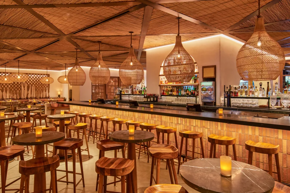 Virgin Hotels Las Vegas Curio Collection by Hilton bar and dining area with woven pendant lights, wooden stools, candlelit tables, and a long counter stocked with bottles.