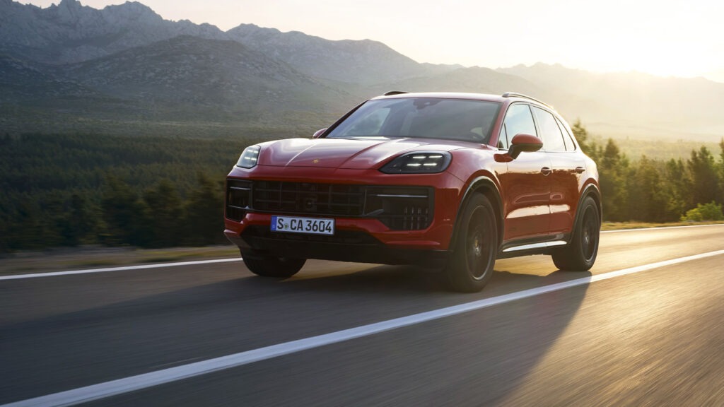 Best Luxury Hybrid SUV shown as a red Porsche Cayenne E-Hybrid driving on an open highway at sunset with mountains in the background.