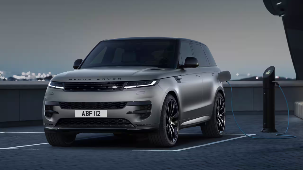 Best Luxury Hybrid SUV shown as a grey Range Rover Sport plug-in hybrid SUV charging at an outdoor EV station at night in a modern parking area.