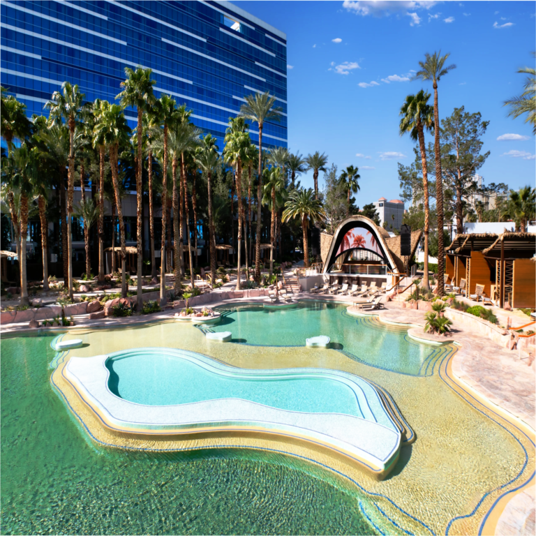 Virgin Hotels Las Vegas Curio Collection by Hilton resort pool with crystal-clear water, palm trees, a poolside stage, and the blue glass hotel tower under a sunny sky.