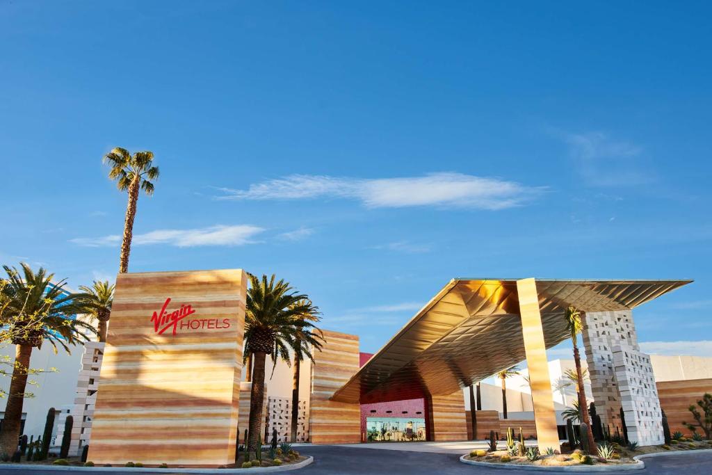 Virgin Hotels Las Vegas Curio Collection by Hilton entrance with modern golden canopy, palm trees, and Virgin Hotels signage under a clear blue sky.