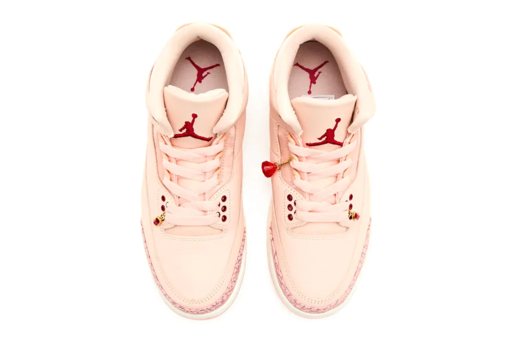 Top-down view of a pink Air Jordan 3 pair with red Jumpman logos and heart-themed lace charms on a clean white background